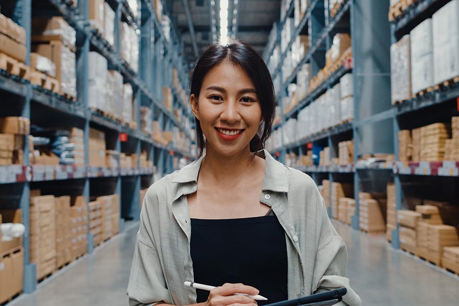 Specialized Business Insurance - Warehouse Manager Surrounded by Shelves of Inventory, Holding a Clipboard and Smiling